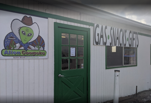 A storefront with a green door and sign reading "Gas, Snacks, Gifts," featuring an alien-themed logo.