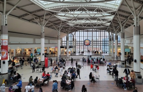A busy indoor shopping area with people dining and socializing under a large glass ceiling.