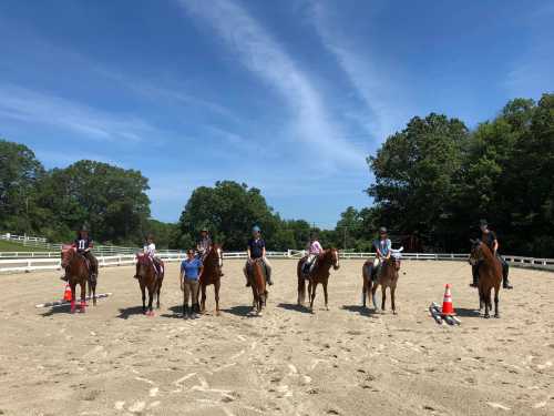 A group of riders on horseback lined up in an outdoor arena under a clear blue sky.