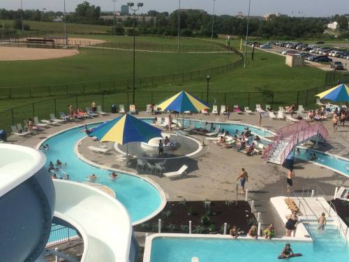 Aerial view of a water park with slides, pools, and people relaxing under colorful umbrellas on a sunny day.