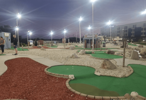 A mini-golf course at dusk, featuring colorful greens, rocks, and illuminated pathways.