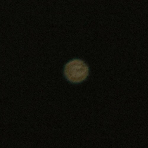 A blurred image of a celestial body, possibly a planet or moon, against a dark background.