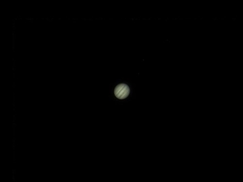 A distant view of Jupiter, showcasing its bands and a few of its moons against a dark background.