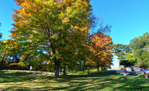 Colorful autumn trees surround the entrance sign of Man Mound Park under a clear blue sky.