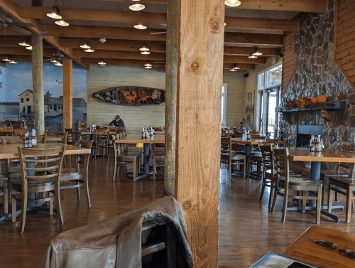 Interior of a rustic restaurant with wooden beams, tables, and a stone fireplace, featuring a few diners.