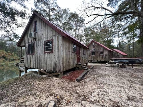 Two rustic wooden cabins with red roofs, surrounded by trees and situated near a calm body of water.
