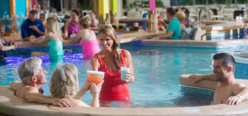 A group of people enjoying drinks in a vibrant pool, with a woman in a red swimsuit serving cocktails.