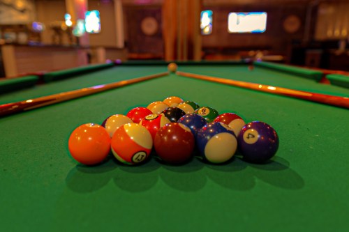 A close-up of a pool table with a triangle of colorful billiard balls arranged on a green felt surface.
