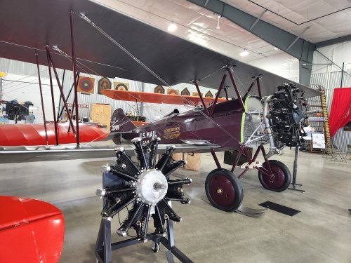 A vintage biplane displayed in a hangar, featuring a red and silver design with a prominent radial engine.