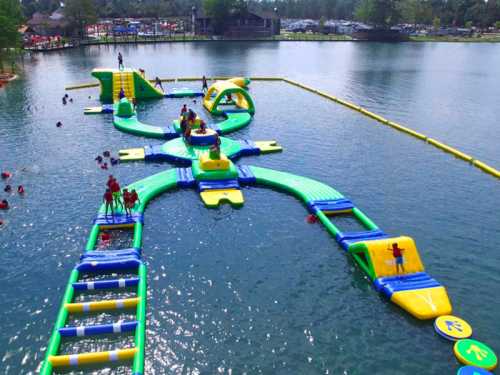 A colorful inflatable water park with slides and obstacles on a lake, filled with people enjoying the summer.