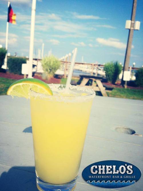 A refreshing margarita with a lime slice sits on a table, with a marina and blue sky in the background.