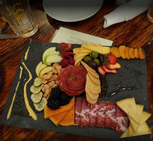A charcuterie board featuring meats, cheeses, fruits, nuts, and sauces arranged on a slate platter.