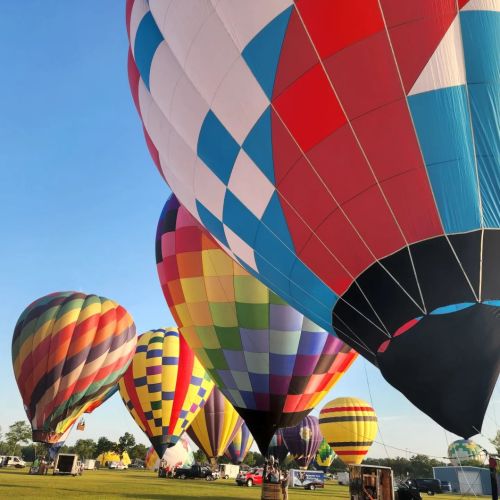 Colorful hot air balloons fill the sky at a festival, with vibrant patterns against a clear blue backdrop.