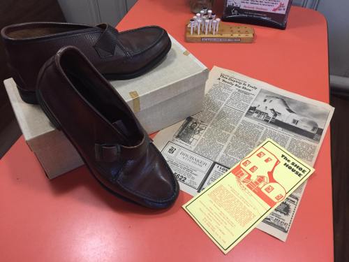 A pair of brown shoes on a table with a newspaper and a flyer nearby.