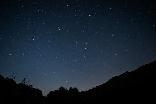 A clear night sky filled with stars, with a dark silhouette of mountains in the foreground.