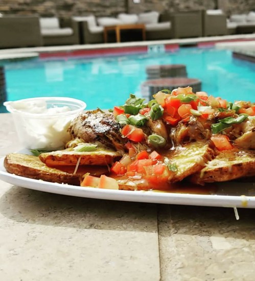 A plate of nachos topped with chicken, tomatoes, and green onions, served with a side of sour cream, near a pool.