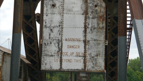 Rusty metal sign with warning text: "WARNING DANGER. FUDGE UP DO NOT GO BEYOND THIS POINT."