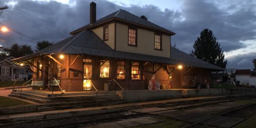 Historic train station illuminated at dusk, featuring a brick exterior and surrounding tracks.