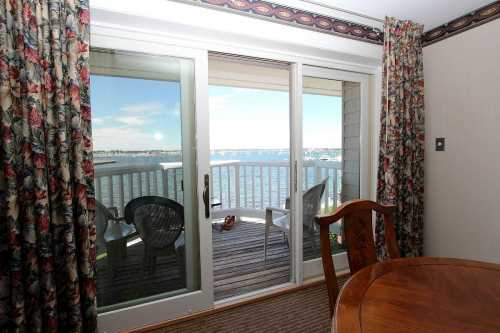 A view of a balcony overlooking water, with a table and chairs inside a room adorned with floral curtains.