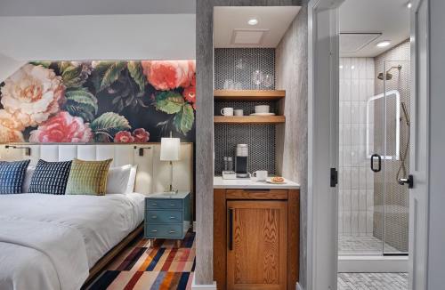 A stylish hotel room featuring a floral accent wall, two beds, a coffee station, and a modern shower.
