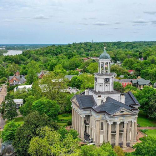 Aerial view of a historic building with a dome, surrounded by lush greenery and a scenic landscape.