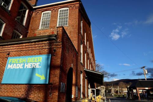 A brick building with a blue sign reading "FRESH BEER MADE HERE" and a clear sky in the background.