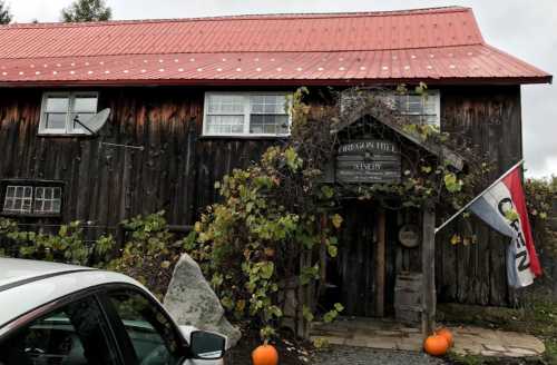 A rustic wooden building with a red roof, vines, pumpkins, and a sign reading "Cider House" at the entrance.