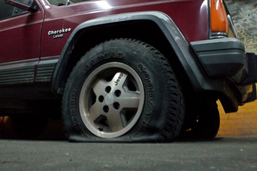 A maroon Jeep Cherokee with a flat tire parked in a dimly lit garage.