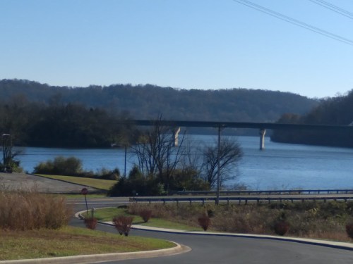 A serene river scene with a bridge in the background, surrounded by trees and clear blue skies.