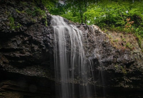 A serene waterfall cascading over rocky cliffs, surrounded by lush green foliage.