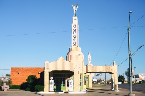 Art Deco gas station with a tall, decorative tower and vintage gas pumps, set against a clear blue sky.