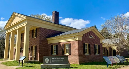 A brick building with a yellow portico, serving as the Visitor Center for Shiloh National Military Park, under a blue sky.