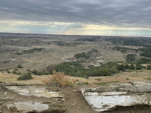 A panoramic view of a rugged landscape with rolling hills, sparse vegetation, and a cloudy sky.