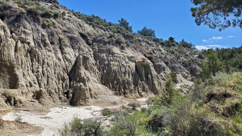 A rugged landscape featuring steep, eroded cliffs and sparse vegetation under a clear blue sky.