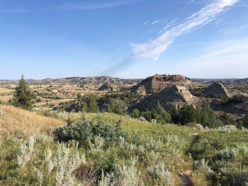A scenic view of rolling hills and rock formations under a clear blue sky, with greenery in the foreground.