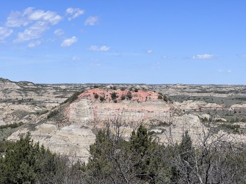 A scenic view of layered hills and valleys under a blue sky, with sparse vegetation in the foreground.