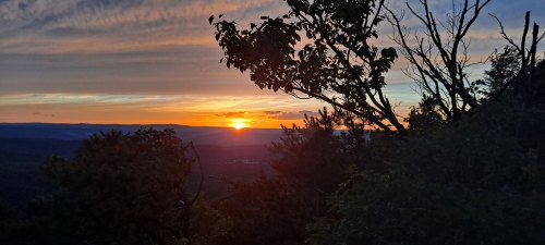 A sunset over a mountainous landscape, framed by silhouetted trees against a colorful sky.