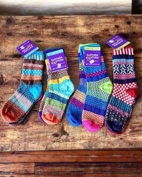 Four pairs of colorful, mismatched socks displayed on a wooden surface, each with unique patterns and designs.