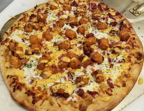 A large pizza topped with cheese, bacon, tater tots, and drizzled with sauce, garnished with herbs.