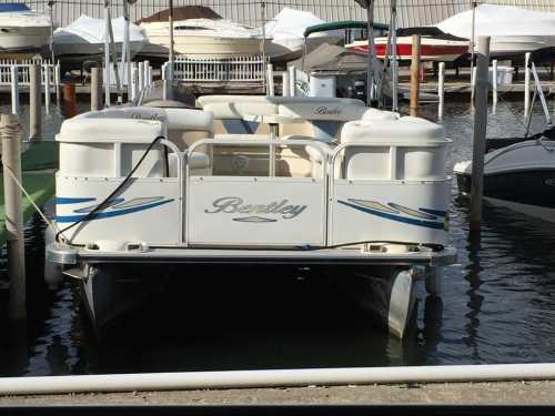 A white pontoon boat named "Bentley" docked at a marina, surrounded by other boats and calm water.