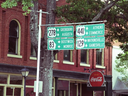 Directional road signs indicating routes to various cities, with a vintage Coca-Cola sign in the background.