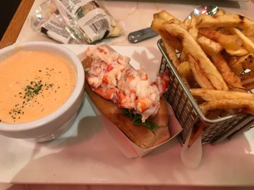 A lobster roll with lettuce, a bowl of creamy soup, and a side of crispy French fries in a small basket.