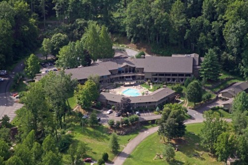 Aerial view of a hotel complex surrounded by trees, featuring a central pool and landscaped grounds.