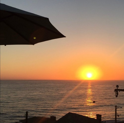 A serene sunset over the ocean, with warm colors reflecting on the water and an umbrella in the foreground.
