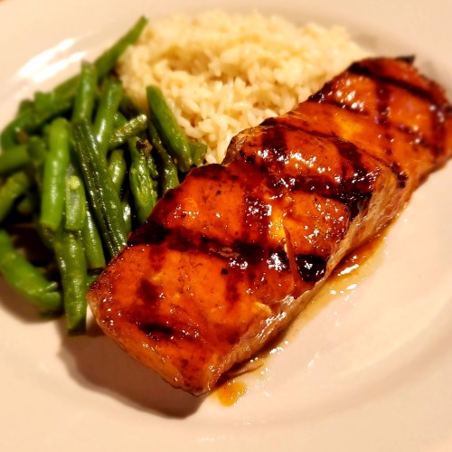 Grilled salmon fillet with a glaze, served with green beans and fluffy rice on a white plate.