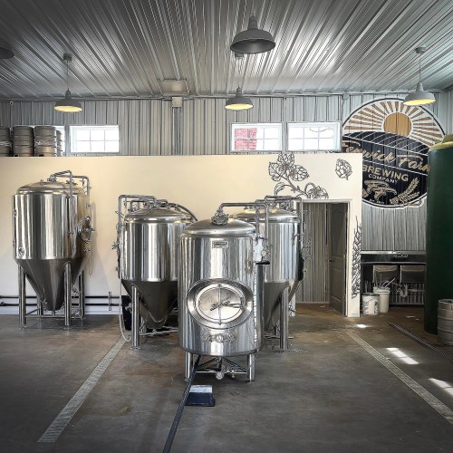 Interior of a brewery featuring stainless steel fermentation tanks and a mural on the wall, with industrial lighting.