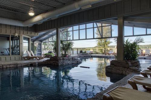 Indoor pool area with natural stone features, large windows, and lounge chairs overlooking a scenic view.