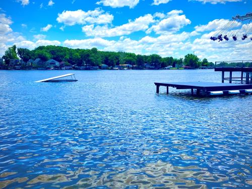 A serene lake scene with a dock, a partially submerged boat, and fluffy clouds reflecting in the water.