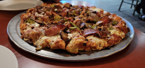 A freshly baked pizza topped with various meats, mushrooms, and jalapeños on a silver serving tray.