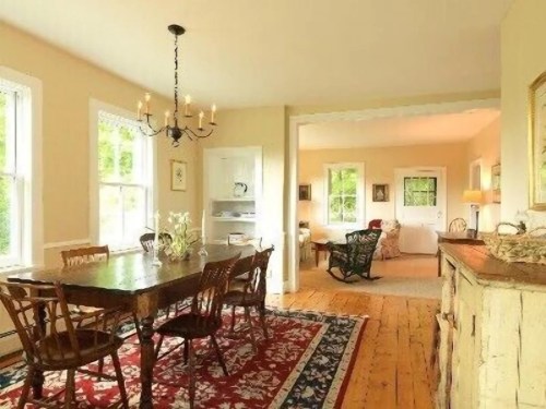 Cozy dining area with a wooden table, chairs, and a chandelier, featuring large windows and warm, inviting decor.